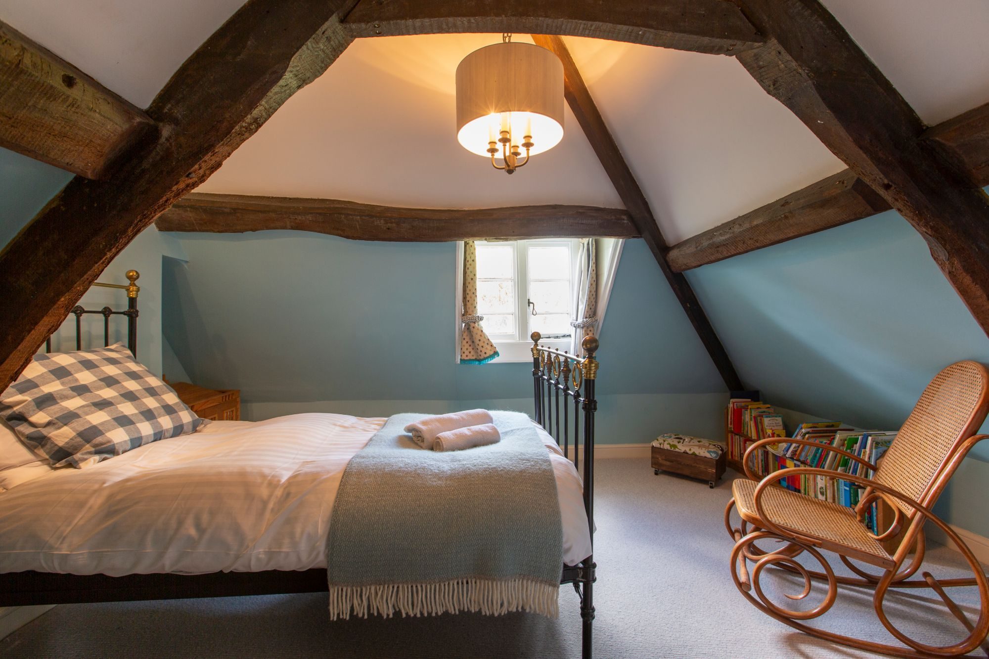 Attic bedroom with exposed A-frame oak beams, duck-egg blue walls and a brass bedstead