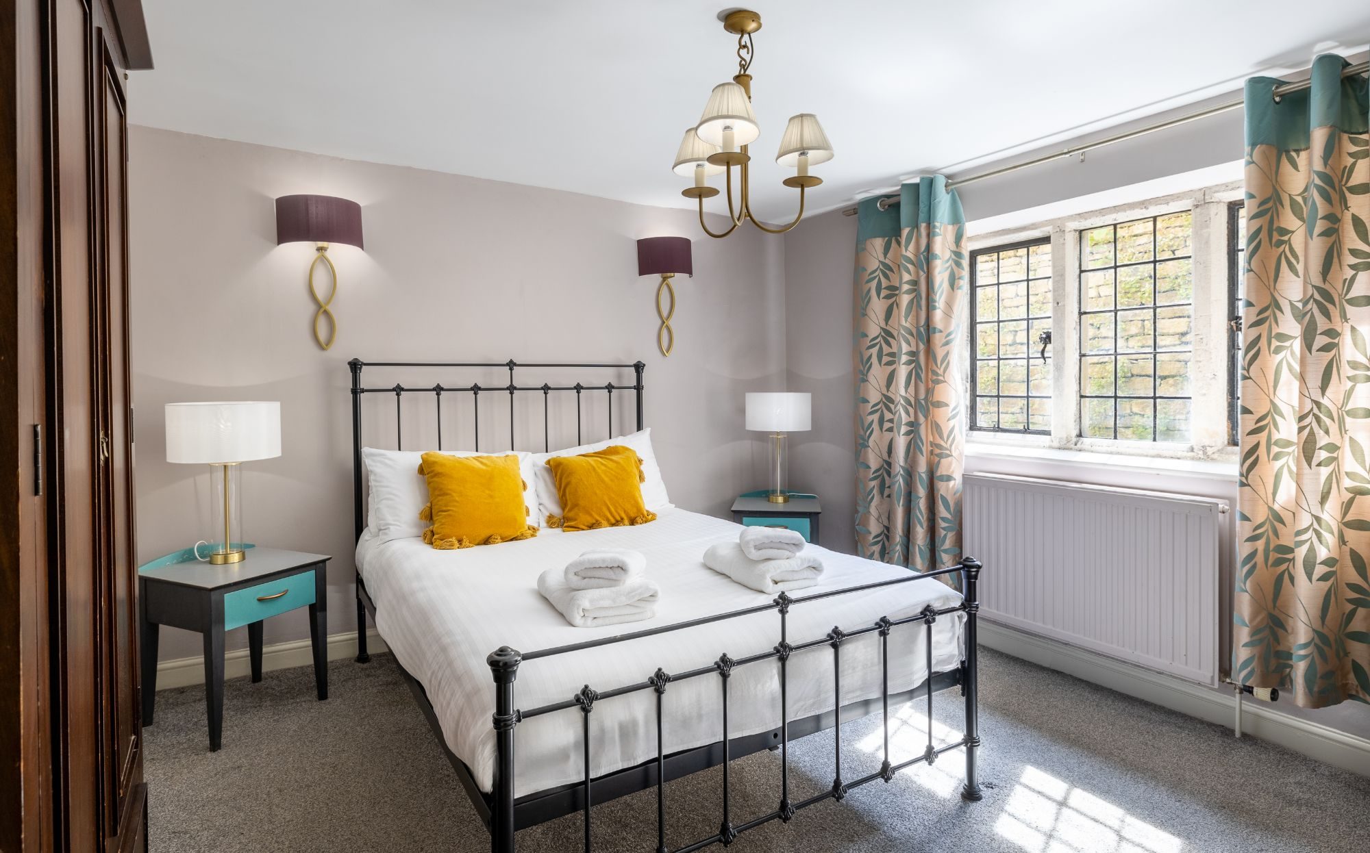 Bedroom with a black iron bedstead, mustard cushions and a stone mullioned window