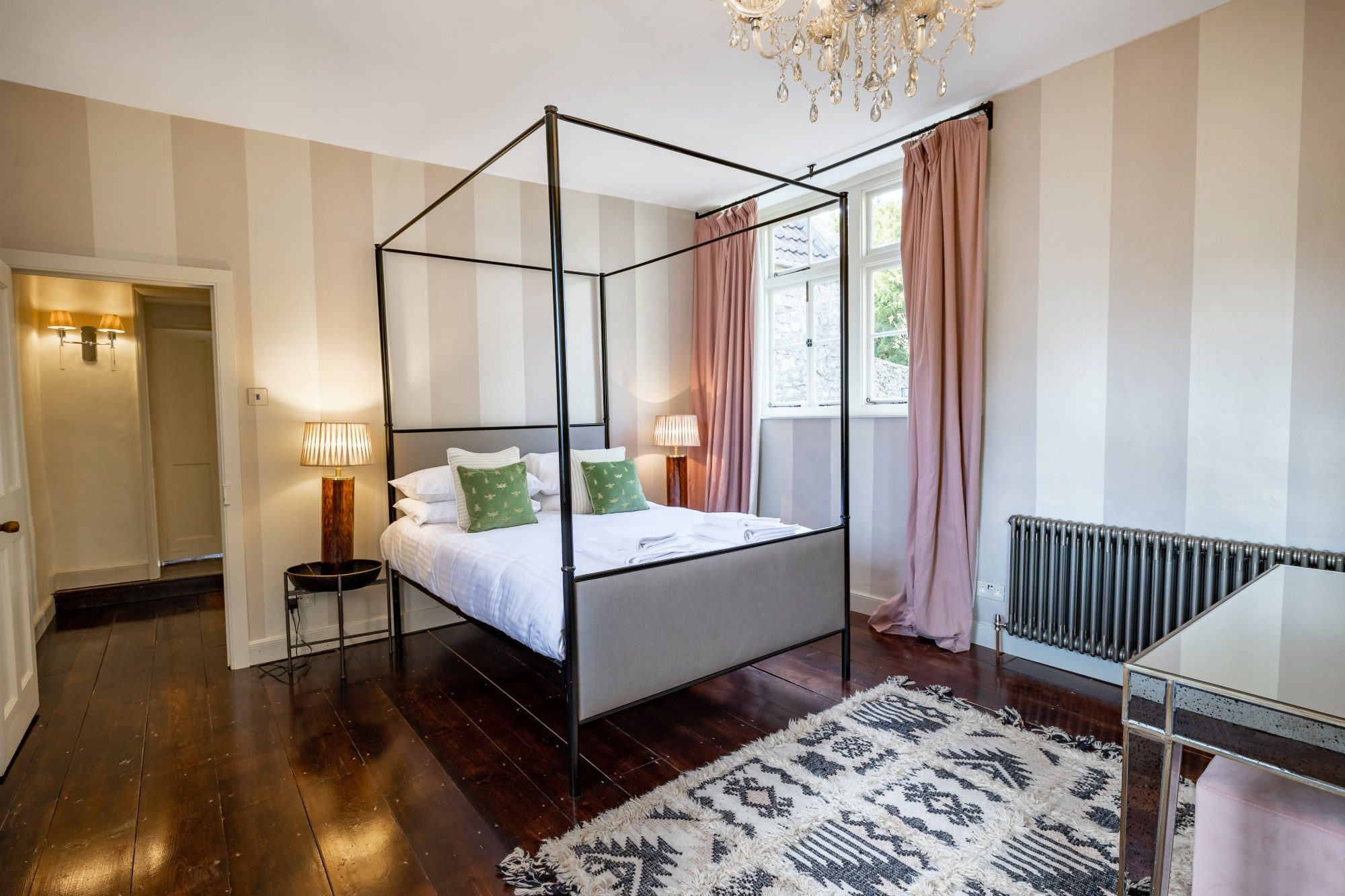 Bedroom with cream and grey striped walls, a black four-poster bed and dusty pink curtains