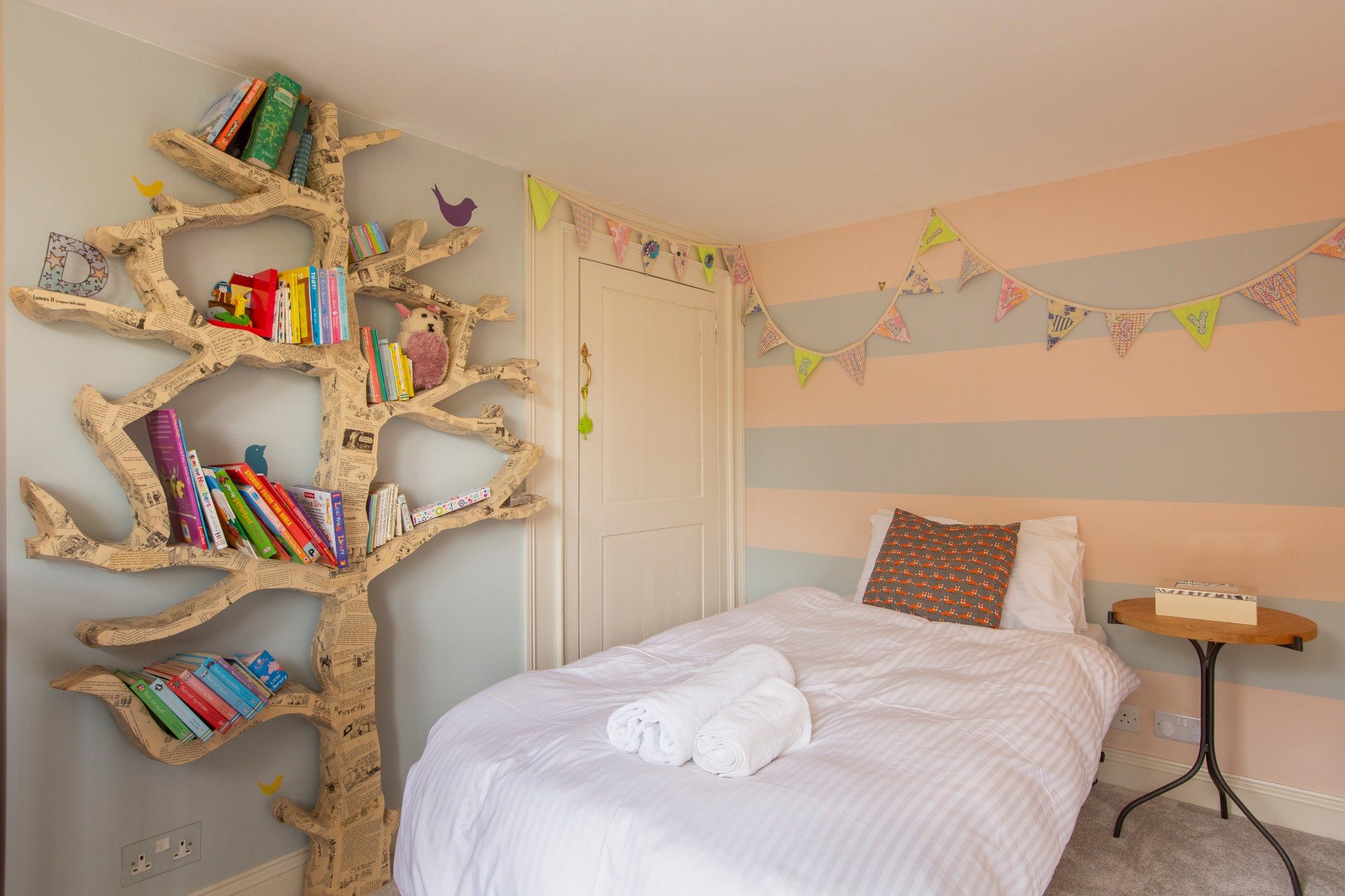 Child's bedroom with a hand-made tree-shaped bookshelf and peach and grey striped walls