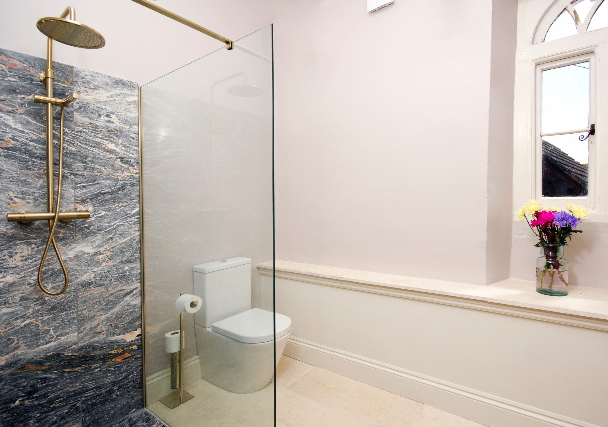 En-suite shower room with brushed brass fittings, a dark marble feature wall and arched window