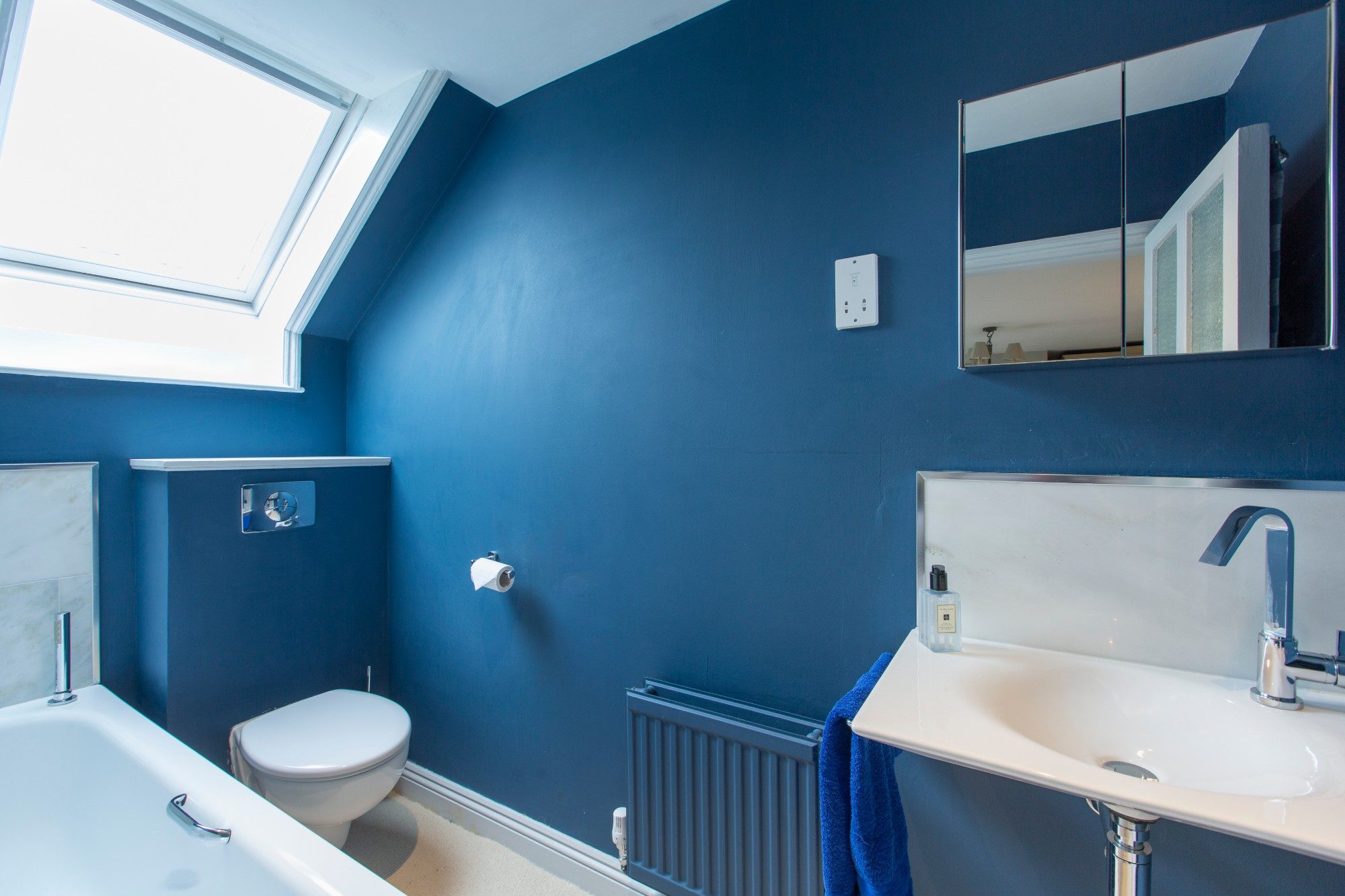 Family bathroom painted deep blue with a skylight, bath and marble splashback