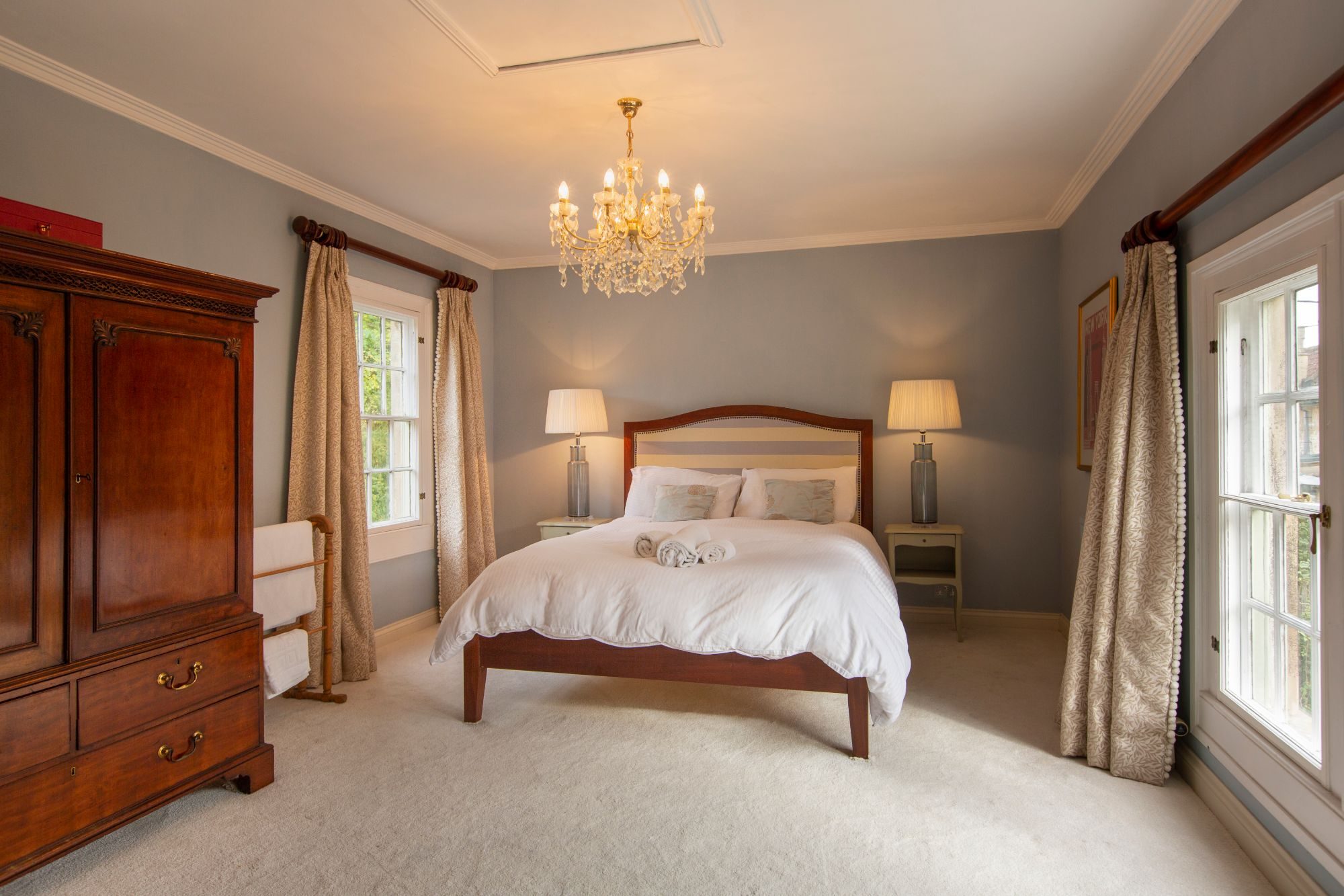 Guest bedroom in soft grey with a crystal chandelier, mahogany wardrobe and sash windows