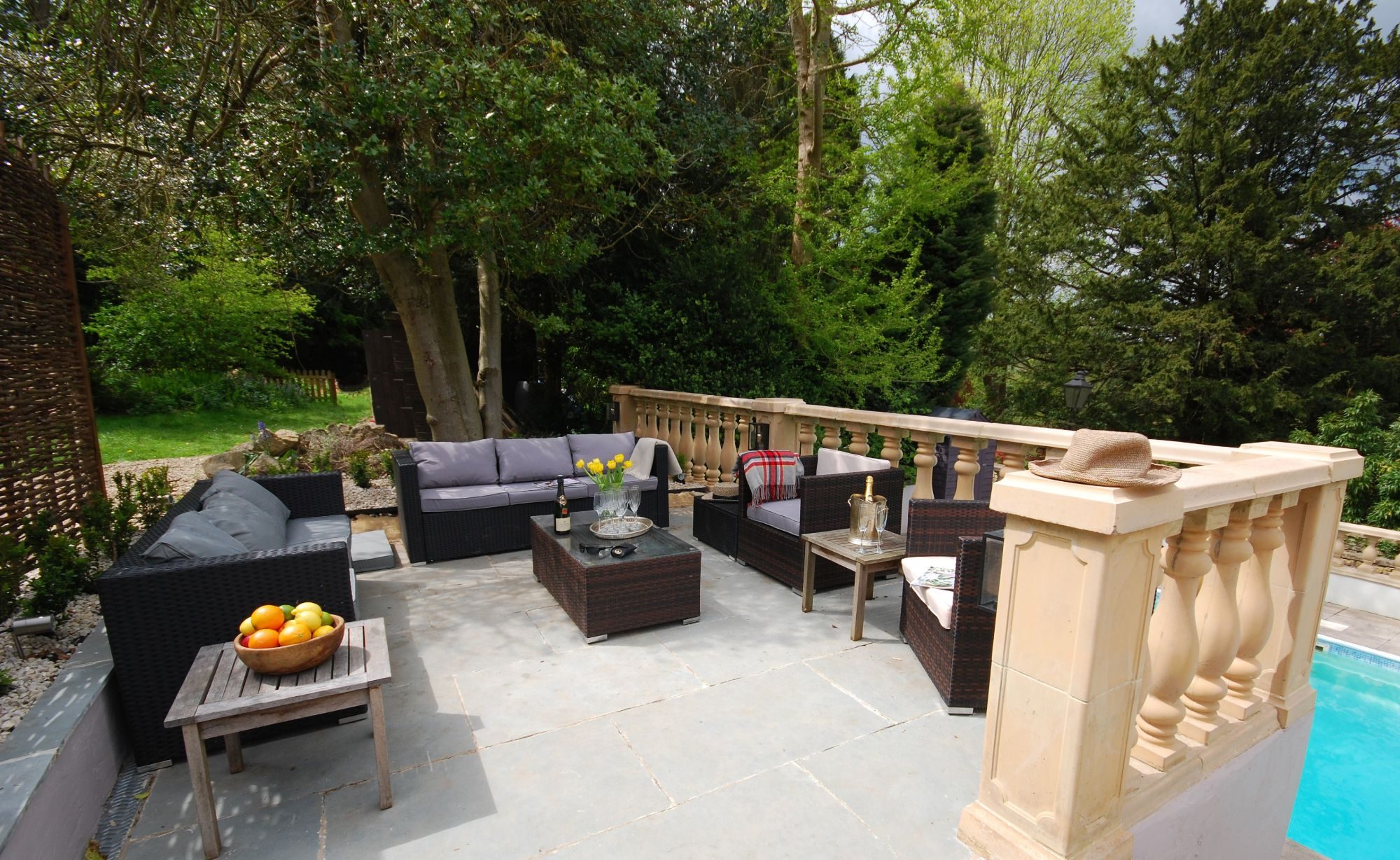Outdoor pool terrace with a carved stone balustrade, rattan seating and mature garden