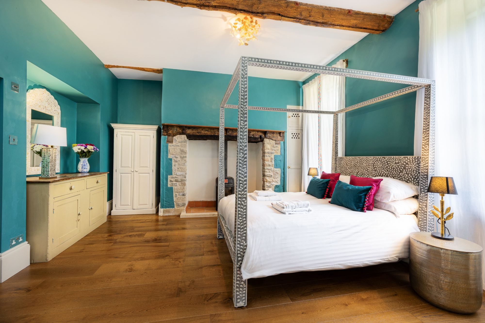 Principal bedroom with deep teal walls, a bone-inlay four-poster bed and exposed oak beams