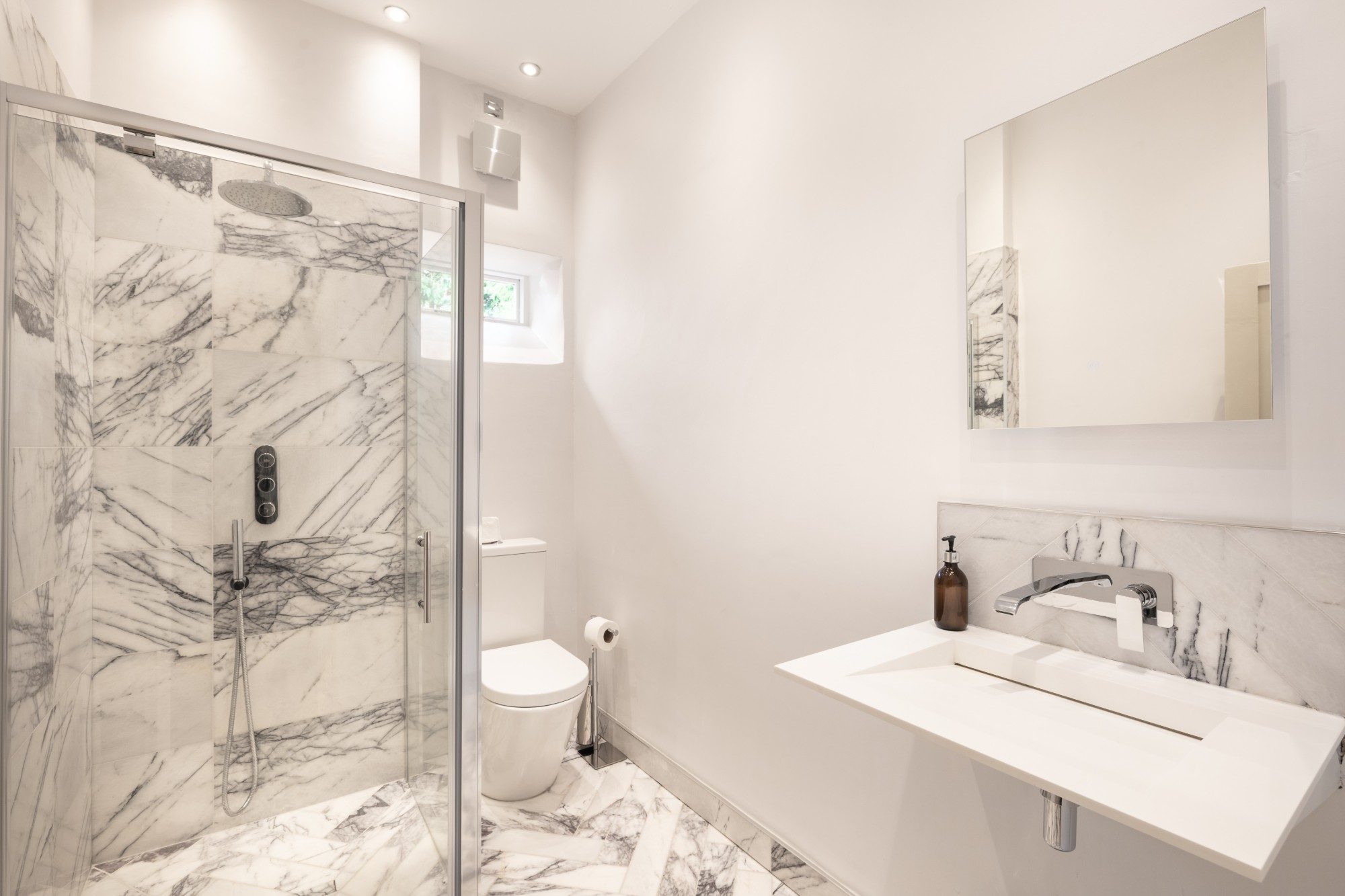 Shower room with white marble walls, herringbone marble floor and chrome fittings