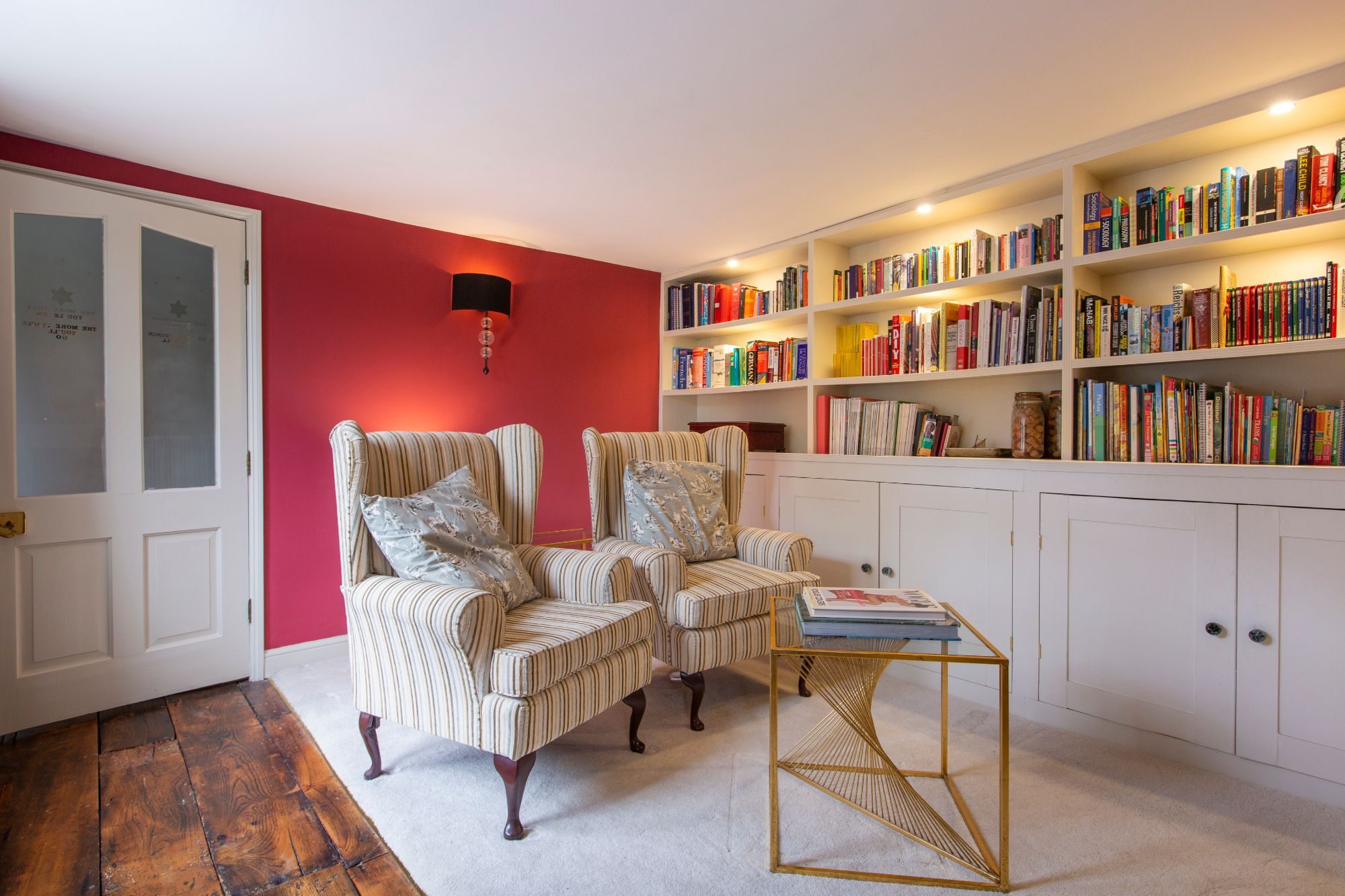 Snug with a crimson accent wall, striped wingback chairs and built-in bookshelves