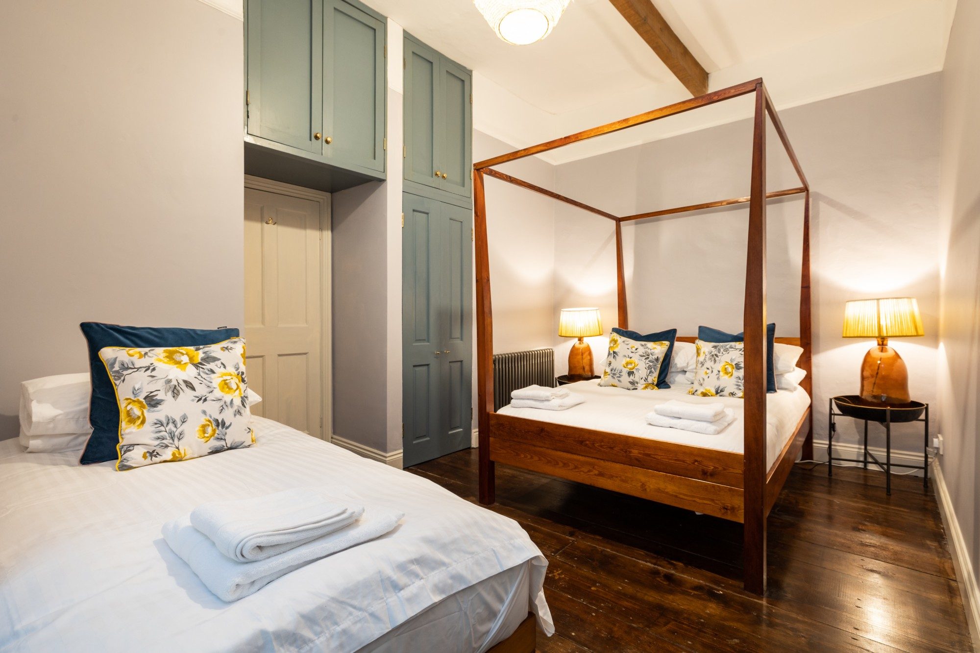 Twin bedroom with an oak four-poster bed, sage green fitted cupboards and exposed beams